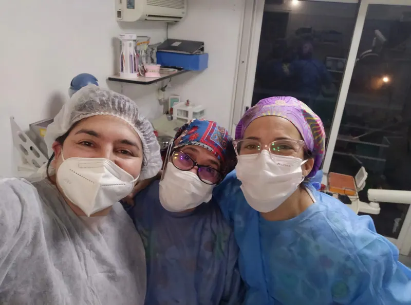 Tres profesionales del equipo, con barbijo y cofia, en el consultorio.